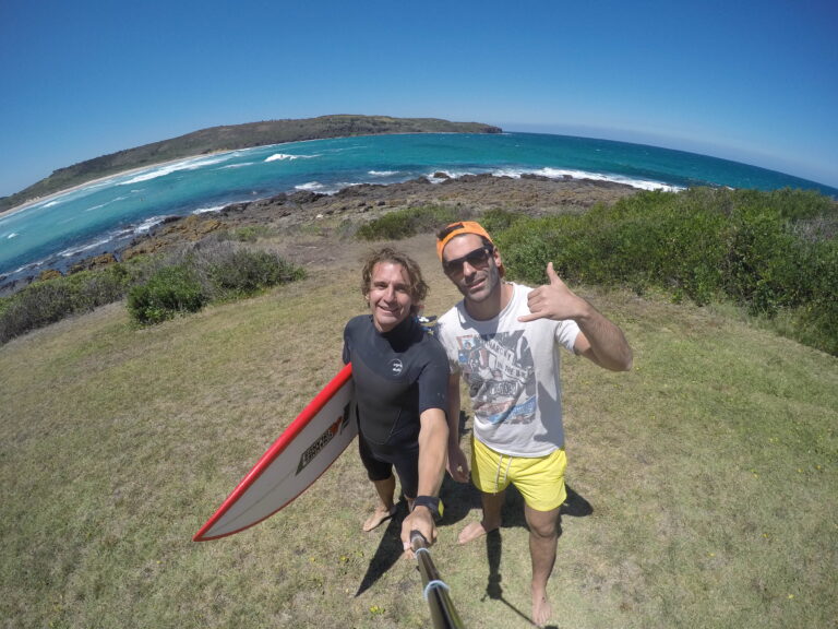 Edu y Alberto, fundadores de Global Way, con una tabla de surf en una playa australiana.